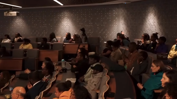 Wide shot of a full Lecture Theatre 1 at King’s College London, audience members seated and looking toward the screen during the FRK film screening.